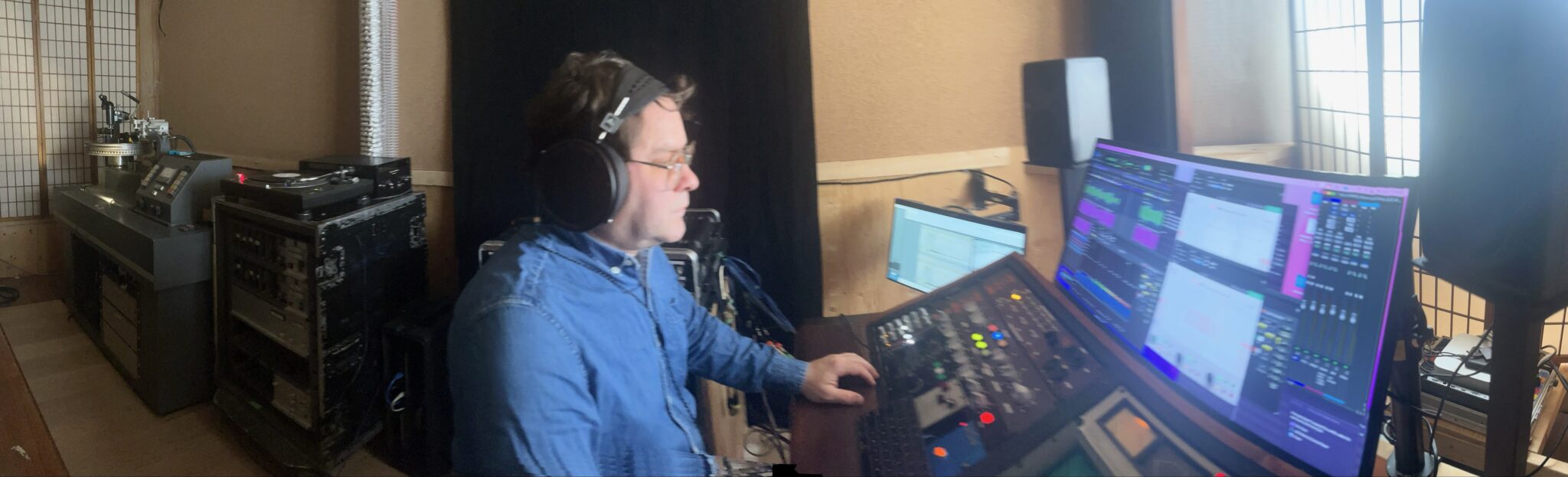 Kevin Park at the mastering desk, wearing headphones, with the lathe behind him